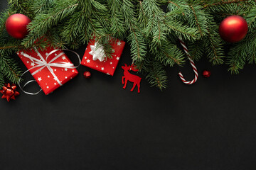 Christmas gift boxes, festive presents composition with copy space on black background. Wrapped gifts, fir tree branches, baubles ornaments and decorations. Winter holiday season flat lay, top view.