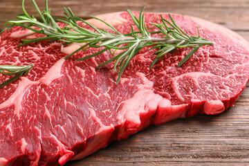 Fresh piece of meat steak with rosemary on wooden table