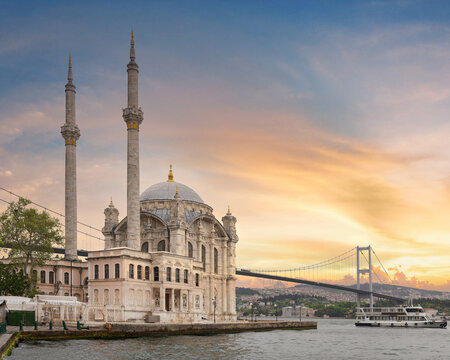 A stunning view of Ortakoy Mosque sitting next to the Bosphorus Bridge with minarets and domes glistening in the rays at sunset in Ortakoy neihborhood, Istanbul, Turkey