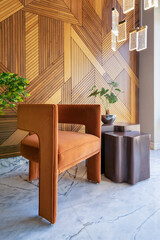 A simple and elegant image of a modern design orange chair and coffe table in front of a decorated wood cladding wall, with hanging lights and a potted plant