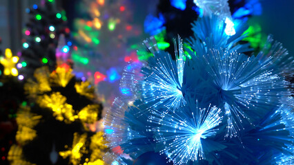 Christmas trees are shining brightly in garlands. Colorful artificial Christmas trees shine with different colors. Coniferous blue, green and white branches. They are decorated with beautiful garlands