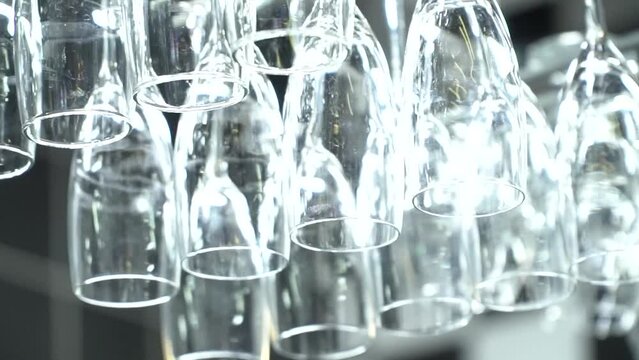 Shiny clean wine glasses hanging on hanger above bar counter, close-up. Empty wine glasses hang upside down in row. Glassware for serving alcohol drinks beverages restaurant business industry concept.
