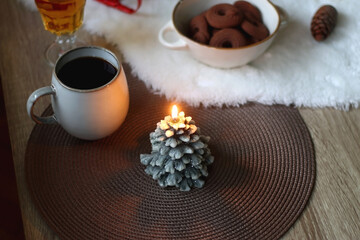 Cup of tea or coffee, glass of wine or juice, bowl of cookies, organic pomegranate, fluffy blanket, pine cones, various Christmas decorations and lit candles on the table. Christmas hygge concept.