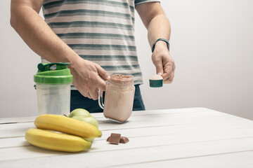 Man holding measuring spoon with protein powder, glass jar of protein drink cocktail, milkshake or...