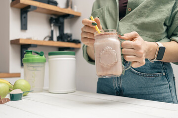 Young woman in jeans and shirt holding glass jar of protein drink cocktail, milkshake or smoothie...