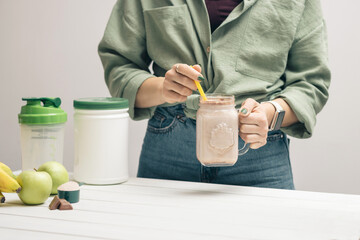 Young woman in jeans and shirt holding glass jar of protein drink cocktail, milkshake or smoothie...