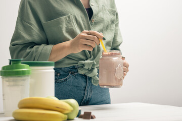 Young woman in jeans and shirt holding glass jar of protein drink cocktail, milkshake or smoothie...