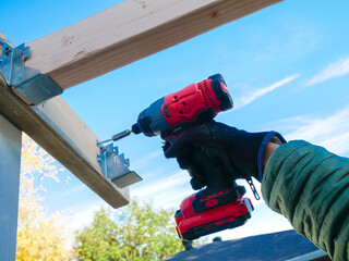 Yellow green fall foliage background, hand man using cordless impact driver fasten attach exterior...