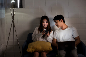 Naklejka premium Asian couple working late from home with a laptop in the dark bedroom. Husband and wife discuss and brainstorm together at night before the business work deadline. Night working, Working late concept.