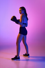 Sporty elegance portrait of strong female boxer, professional MMA sportsman against gradient pink-violet studio background in neon light.