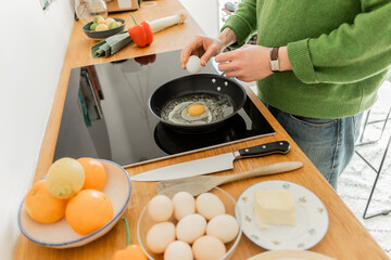 Cropped view of tattooed man holding egg near frying pan while cooking breakfast near butter