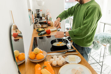 Cropped view of bearded man seasoning fried eggs with peppercorns from mill
