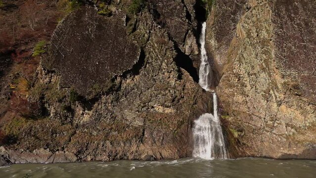 Majestic scenery of huge rock and tiny waterfall flowing from it into lake filmed in slow motion at day time. Landscape of cascade streaming from cliff. Amazing nature of Mingrelia region in Georgia