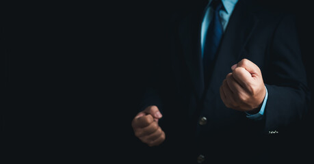Businessman in a suit stands and makes a fist gesture on a dark background.