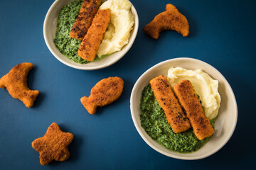 Gebratene Fischstäbchen und Figuren als Fisch, Seestern und Delfin für Kinder mit Rahmspinat und Kartoffel Püree in Schale mit dunkel blau Hintergrund © Christin Klose