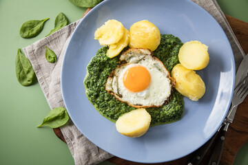 Rahmspinat mit Salzkartoffeln und Spiegelei auf Emaille Teller mit Besteck, Holzbrett, Serviette,...