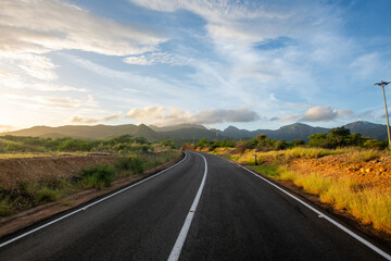 Fototapeta premium Sunrise in the desert. Tour of a desert island, full of xeric vegetation. Cactus and red earth. Mountains, clouds and sun