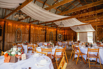 A wedding barn venue with decorated tables, fairy lights and draping chiffon hanging on top.