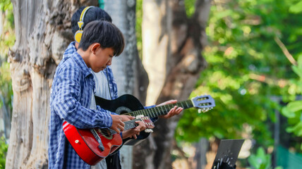 Young Asian boys are playing acoustic guitars in front of a house, soft and selective focus                               - obrazy, fototapety, plakaty