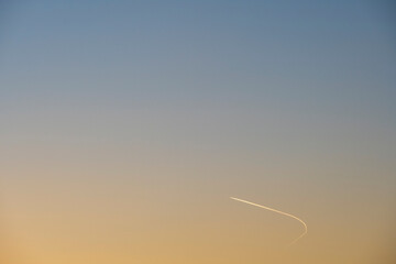 An airplane makes a turn in the orange-blue sky at sunset. Sunset in the sky.  Minimalism.