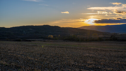 Sunset over the mountain. The sun's rays fall on the plowed fields and on the forest at the bottom of the mountain.