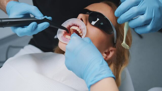 Dental practitioner surgeon with female assistant examine and clean young woman's oral cavity. Teeth correction. Stomatology clinic. Medical procedure. Dentist.