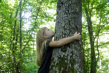 Cute little girl hugging tree. Hugging and touching trees provide rich sensory experience for...