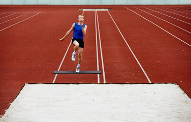 Take off. Focused runner propelling into sand pit. Young man, professional sportsman pushes off...