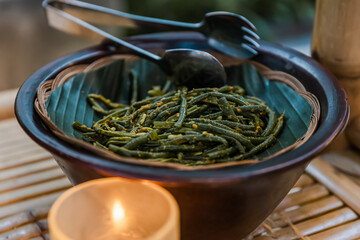 Close up side view of steaming hot spicy szechuan green beans on white plate and wood surface