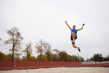 Strategic takeoff for successful long jump into sand. Dynamic photo of professional sportsman...
