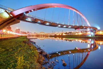 The famous Rainbow Bridge over Keelung River with reflections in the water at blue dusk, in Taipei,...
