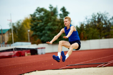 Graceful arch as a runner jumps into sand. Dynamic portrait of athletic man, professional sportsman...