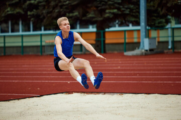 Precision and poise define athlete's descent into sand. Athletic man, professional sportsman sets...