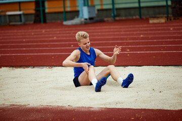 Controlled descent into sand, showcasing finesse of skilled long jumper. Young man sits in sand court after well done long jump.