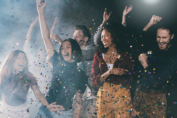 Group of happy young people dancing and throwing confetti while having fun in night club together