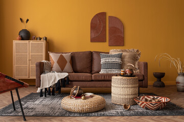 Warm and cozy composition of african living room interior with mock up poster frame, brown sofa,...