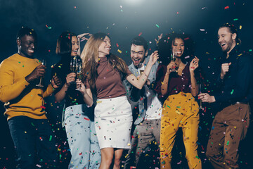 Group of smiling young people dancing and throwing confetti while enjoying party in the night club