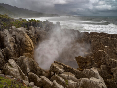 High tide and a strong swell produce a blast of ocean mist at a rocky blowhole; Greymouth, Punakaiki, South Island, New Zealand