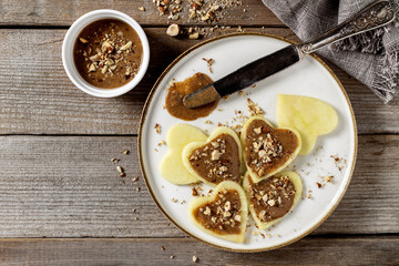Heart shaped apple slices with hazelnuts and butter spread top view on wooden table