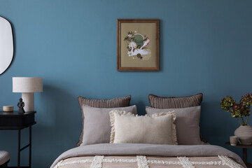 Warm and cozy bedroom interior with mock up poster frame, bed, gray bedding, stylish pillows, vase with flowers, bedside table, lamp, blue wall and personal accessories. Home decor. Template.