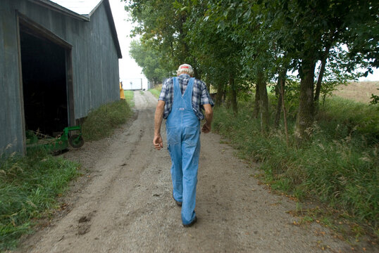 Senior man walks down a dirt road on a farm; Cortland, Nebraska, United States of America