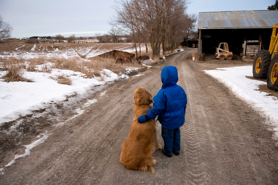 Young boy stands in a gravel road with a golden retriever; Cortland, Nebraska, United States of America