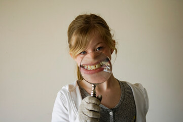 Girl emphasizes her smile with a magnifying glass on a white background; Studio