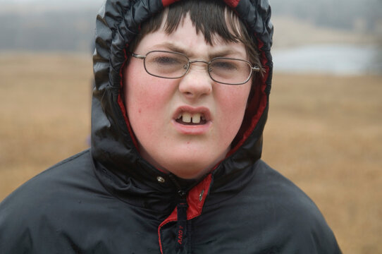 Boy standing outside in a foggy field with his hood up, looking at the camera with a disgusted face; Lincoln, Nebraska, United States of America