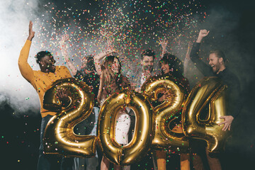 Group of happy young people celebrating 2024 New Year while throwing confetti in night club