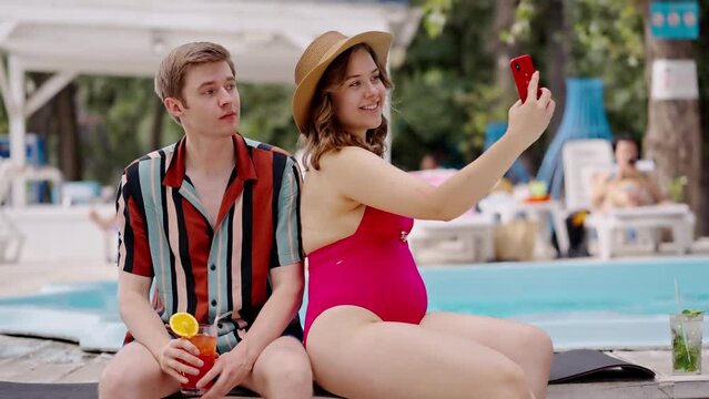 Bored guy must photographing with girlfriend at joint rest at poolside. Young body positive girl ask boyfriend pose when she blogging in swimming pool. Lady in bodysuit recording video with boyfriend