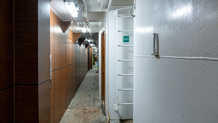 Interior of a ship deck corridor with wooden doors and white walls.