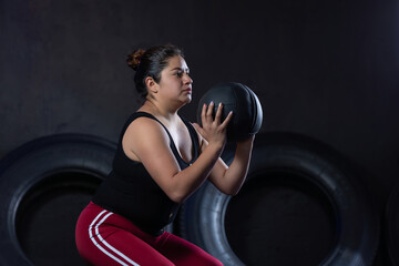 Young Overweight Mexican woman holding a gym ball in sports clothes, new year's resolutions