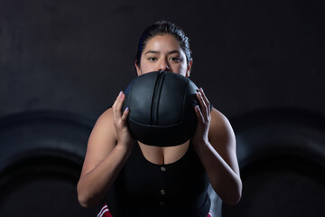 overweight Mexican woman holding a slam ball, in a black gymnasium new year's resolutions