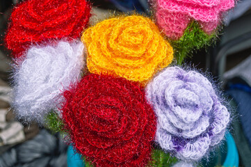 Handmade yarn flowers. A bouquet of flowers knitted from yarn. A background of multicolored flowers. Products made from skeins of yarn. Handmade decoration. A gift for the holiday. Festive mood.